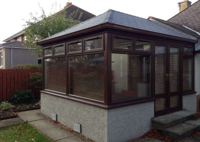 Another Conservatory with brown window frames grey tiled roof and steps in garden